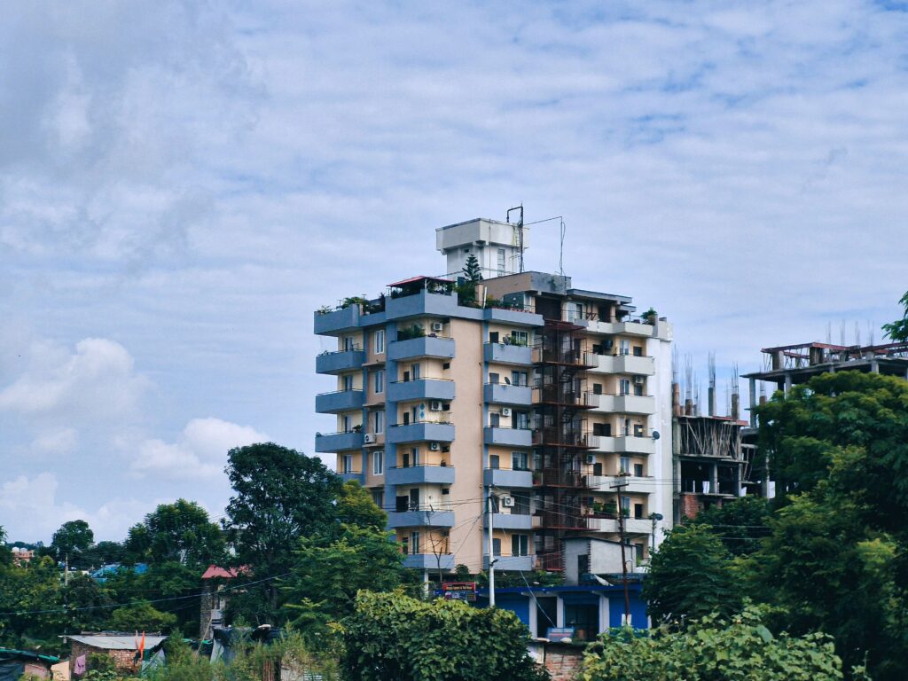 High-rise apartment building in Dehradun, India, with lush greenery and blue sky background.